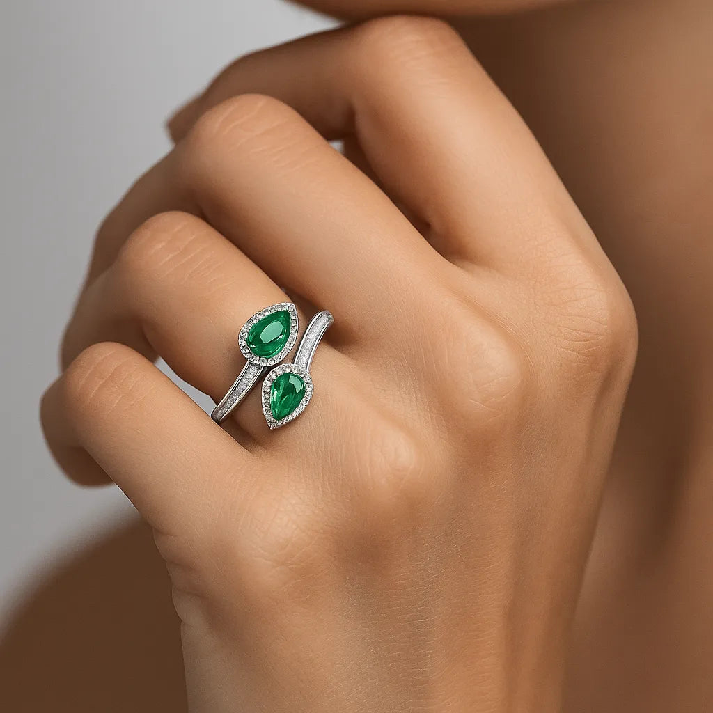 Silver ring with green gemstones on a hand against a neutral background