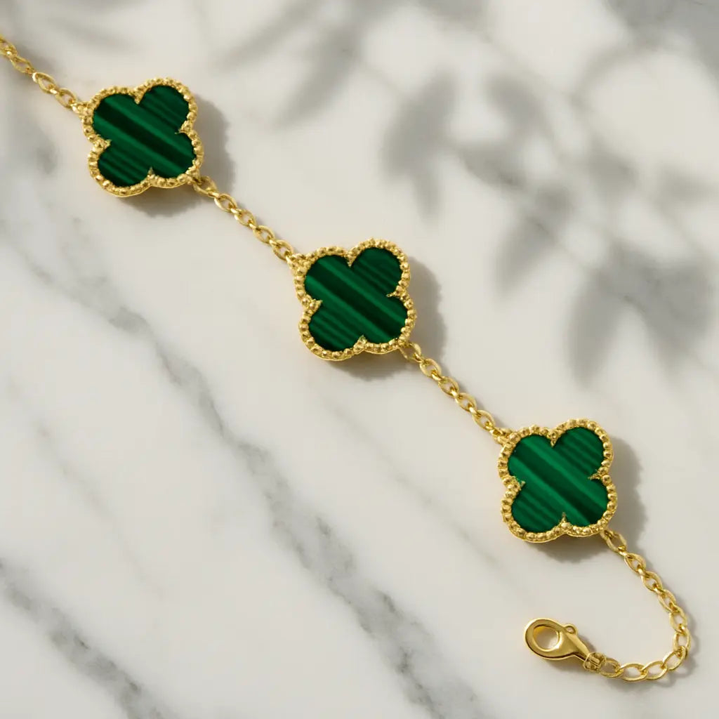 Gold bracelet with green clover-shaped stones on a marble surface