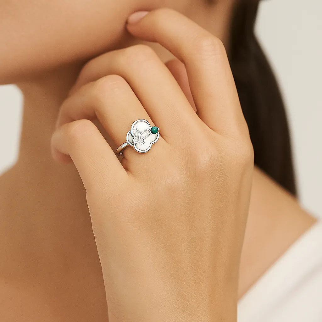 Hand wearing a silver ring with a green gemstone on a neutral background