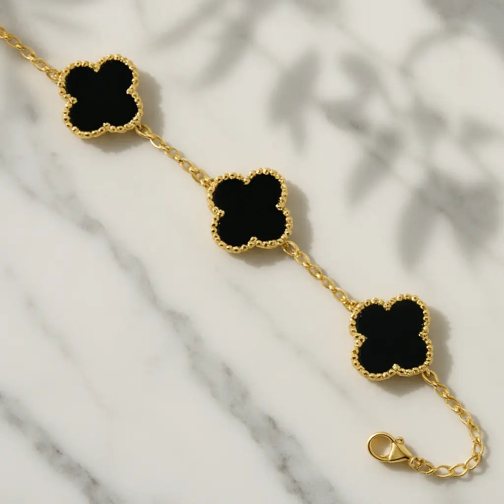 Gold bracelet with black clover-shaped charms on a marble surface