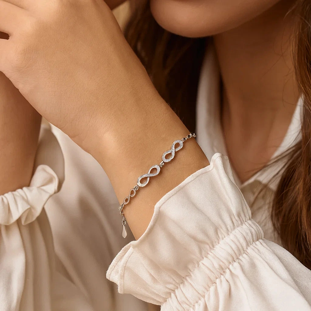 Close-up of a person wearing a silver bracelet with infinity symbols on a blurred background.