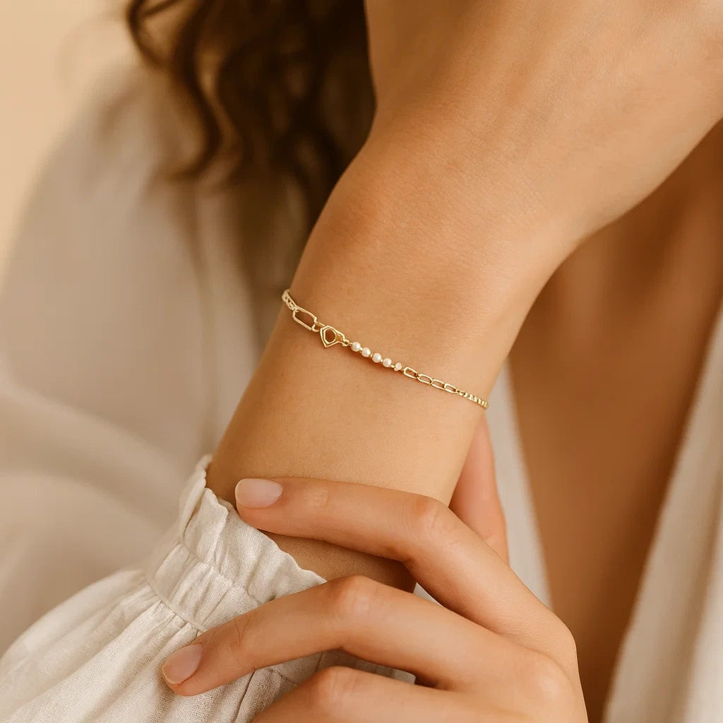 Gold bracelet with pearls on a wrist against a neutral background