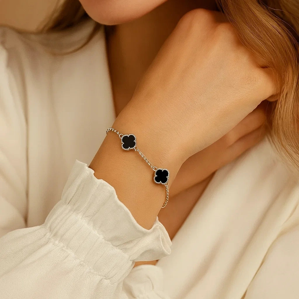 Close-up of a person wearing a silver bracelet with black clover charms on a neutral background
