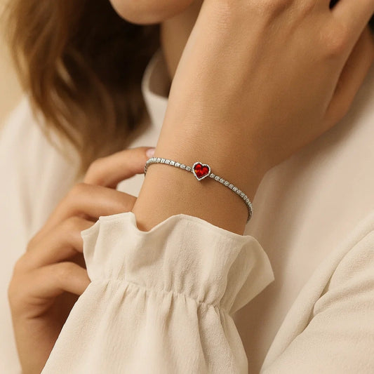 Close-up of a person wearing a bracelet with a red heart charm on a neutral background