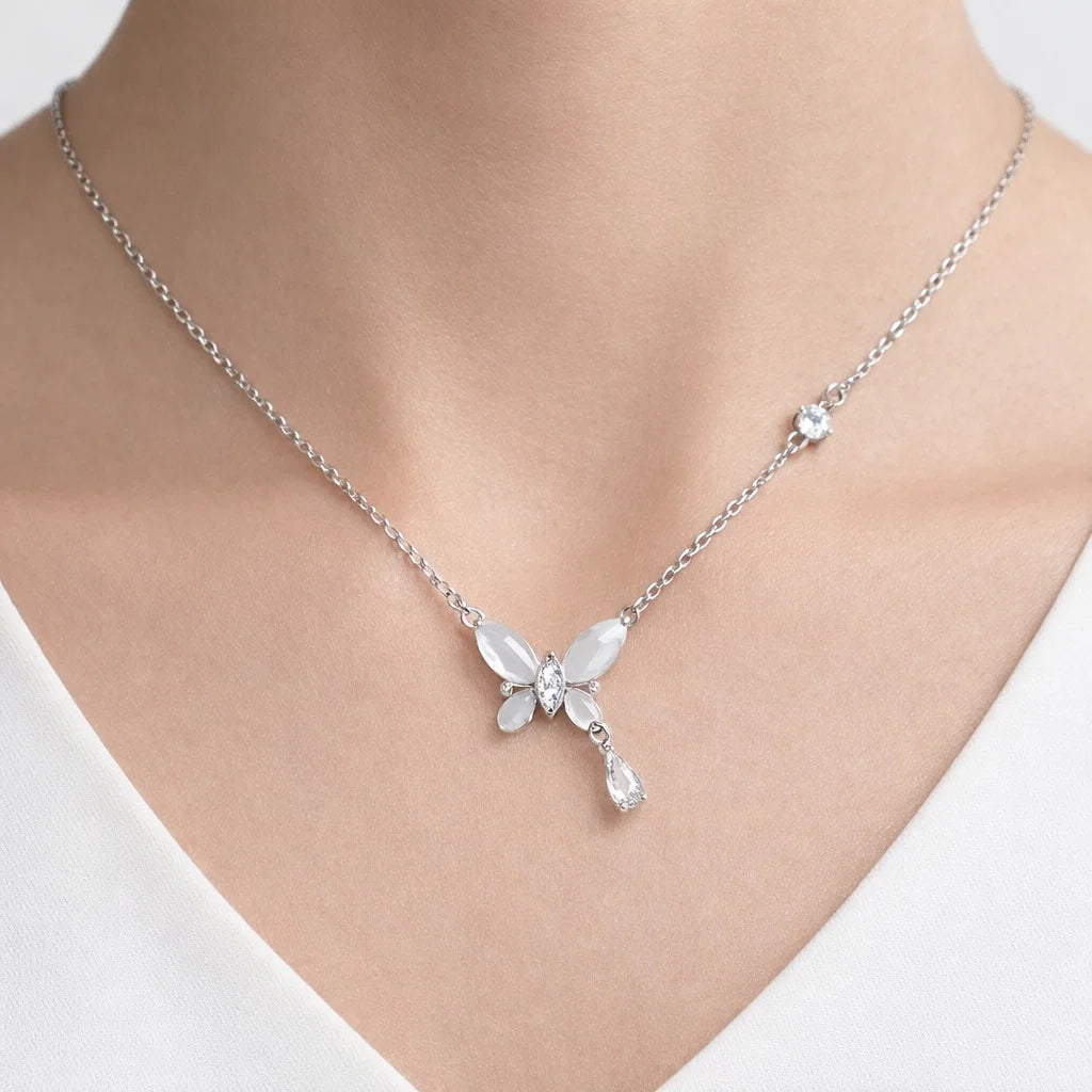 Silver necklace with a butterfly pendant on a person wearing a white top.