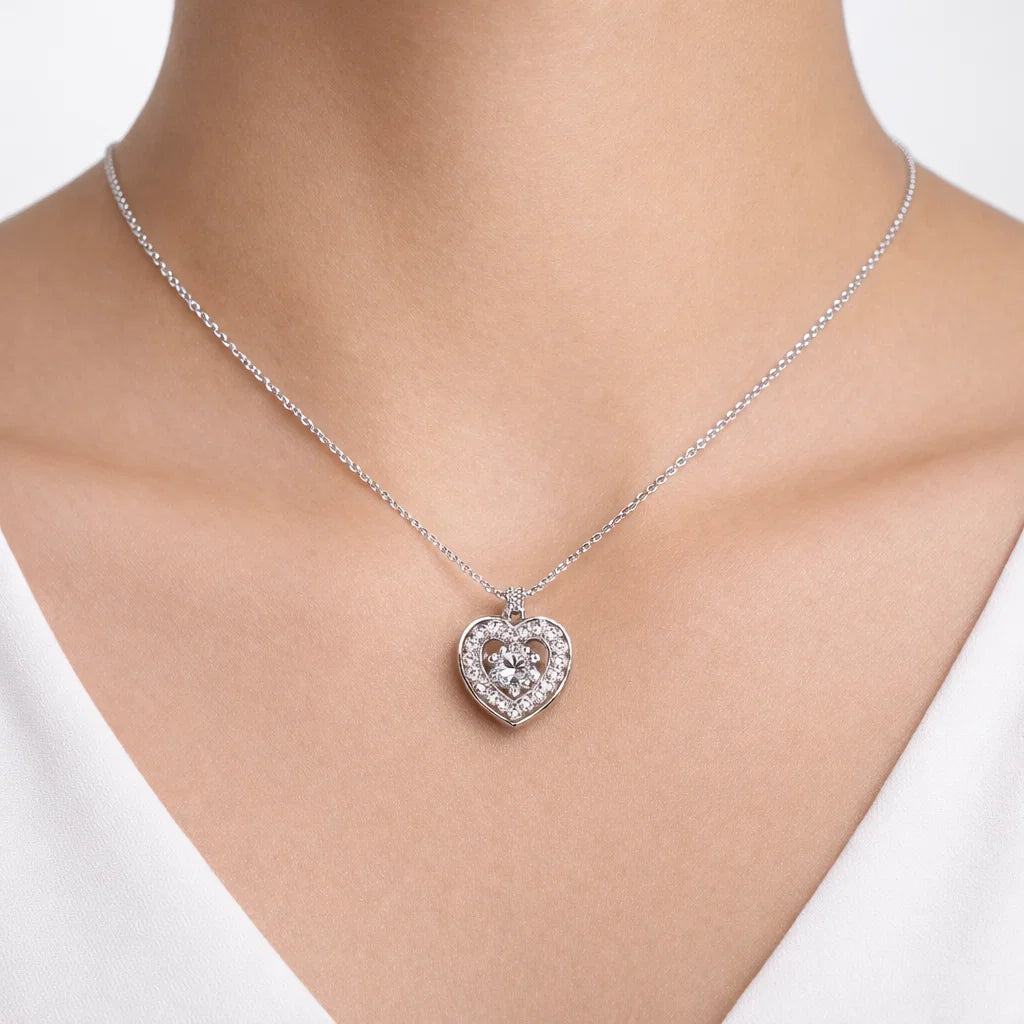 Silver heart-shaped necklace with clear stones on a model wearing a white top.